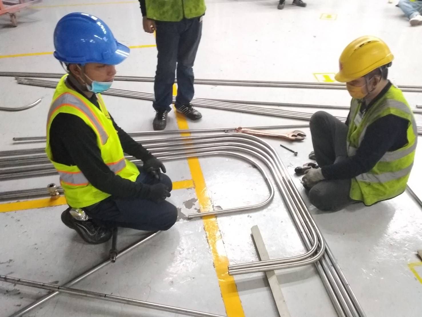 Two workers in hard hats and safety vests bending conduit on a factory floor
